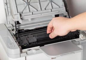A man takes out a cartridge from a laser printer for maintenance and refilling toner, close-up photo