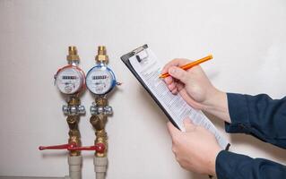 A man writes down the readings of water meters with a pen on paper. The concept of paying for utilities. Rise in price per cubic meter of water photo
