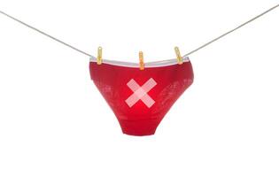 Women's red panties with a cross hanging on a clothesline, white background, isolate. Concept of proctological diseases in women, coloproctology photo