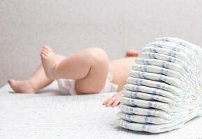 A little caucasian baby boy in a diaper lies on a white background and plays with a bunch of diapers. Copy space for text photo