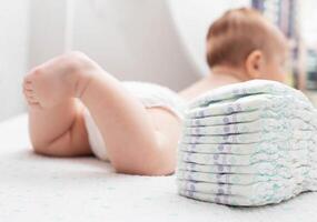 The legs of a baby in a diaper against the background of a stack of children's comfortable diapers, close-up photo