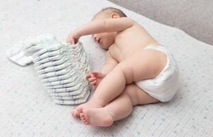 A little caucasian baby boy in a diaper lies on a white background and plays with a bunch of diapers. Copy space for text photo