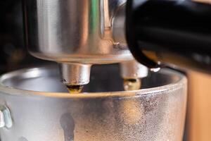 Hot coffee flows out of the espresso machine into a transparent mug, macro. Yummy photo