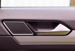 Modern car door trim with tweeter and door handle with metal insert, close-up photo