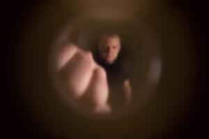 View from the peephole. Angry male neighbor knocking on the front door with his fist, close-up. Blurred photo