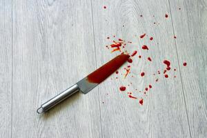 A knife with blood spatter lies on the linoleum, close-up. Concept of crime, robbery and theft. Copy space for text photo