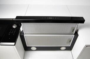 A modern black cooker hood in a white kitchen with a grease and charcoal filter. Air absorption photo