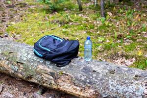 Things in a backpack and a bottle of water are on a tree in the forest. Concept kit for survival in the forest. photo