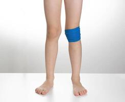 Blue elastic bandage on the knee joint on the child's leg. White background, treatment of knee pain and sprain, close-up photo