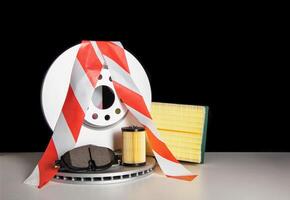Car parts on a black background with a red white ribbon. The concept of restrictions on the import of auto parts from Europe. Sanctions in the automotive business, copy space for text photo