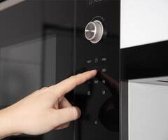 A man's hand presses the touch panel of a modern microwave oven to select the power and function of heating food. Close-up photo