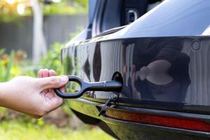 A man twists a towing eyelet into a passenger car to pull the car out of the mud, close-up photo