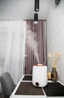 A modern humidifier sits on a table in a kitchen room. Humidification in the room, comfortable humidity and temperature photo