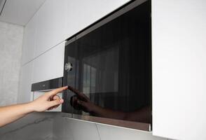 A man presses his finger on the touch panel of a microwave oven to turn on the defrost function. High tech modern microwave oven photo