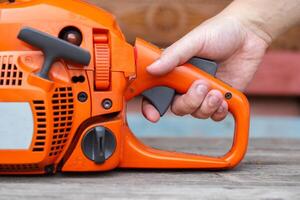 The man's hand presses the gas button in the chainsaw. The concept of adjusting the chainsaw carburetor and testing the power and throttle response. Industry photo