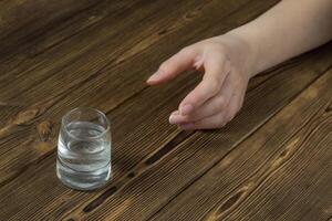 A woman's hand reaches for a wine-glass with alcohol, a wooden background, a close-up, a ghastly alcoholism photo