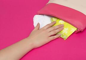 The girl reaches out to her purse in which the women's daily pads for critical days lie, pink background, copy space photo