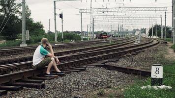 man is sitting on the railway or railroad and talkIng on the smartphone, life threatening photo