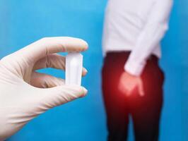 A doctor holds a healing suppository from problems with the rectum and hemorrhoids, the man holds on to the anus of the problem with hemorrhoids and anal fissure photo