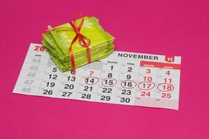Calendar with days marked with a red felt-tip pen and a stack of pads, pink background, menstruation frequency, copy space photo