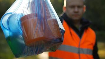 A man in a signal orange vest holds a package with garbage on the background of nature, forest, close-up, garbage collection, a janitor, volunteer, rubbish photo