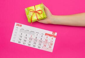 Calendar with marked days of menstruation in a girl, female hand with a stack of sanitary pads, pink background, period, pms photo