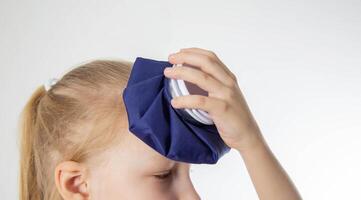 A little girl holds a bag of ice cold against her head. The concept of applying a cold compress to bruises and bumps on the head, close-up. Local cryotherapy photo