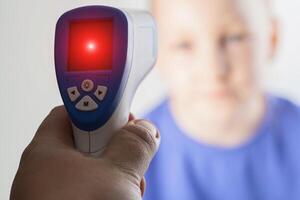 A red spot on a non-contact thermometer when measuring the body temperature of a girl and child. Concept of high temperature for flu and bacteria, close-up photo