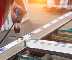 Production of pvc windows, the worker is screwed with a screwdriver with a snap to the pvc window, close-up, screwdriver photo