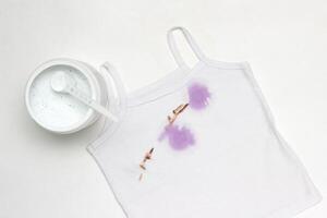 Children's white T-shirt with spots, next to the container with stain remover, close-up, white background photo