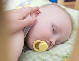 Mother stroking a sleeping baby with a pacifier photo