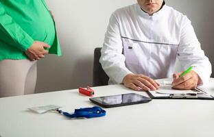 The doctor writes a prescription for medicines and a referral to the hospital for a pregnant girl who has multiple pregnancies and impaired fetal development. photo