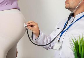 Doctor obstetrician gynecologist using a stethoscope for pregnant women listens to the mobility and heartbeat of the fetus in the womb, unrecognizable photo
