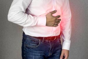 A man in a white shirt holds on to the abdomen, abdominal pain, heartburn, close-up photo