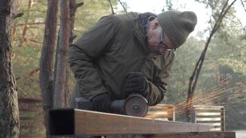 A craftsman is focused on cutting metal with a grinder in a wooded area. Sparks are flying as he shapes the material, showcasing dedication to his craft in nature. video
