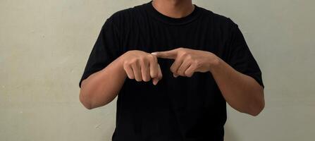 Young man showing word TIME in sign language on gray background photo