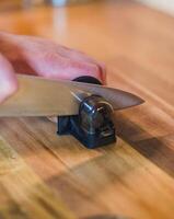 Close-up hand sharpening a knife with a handheld sharpener on a wooden surface. High quality photo