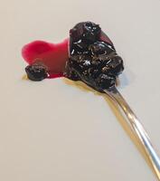 Spoon with a heart-shaped spill of dark red jam, with berries on a light surface. High quality photo