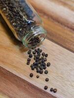 Black Peppercorns Spilled from a Glass Jar on wooden background. High quality photo