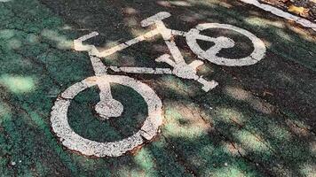 Bike Lane Symbol A close-up shot of a white bike lane symbol painted on asphalt, with dappled sunlight creating a natural bokeh effect. This image conveys a sense of motion, freedom. video