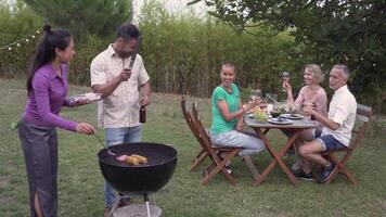 Multiracial mature people cooking corn and meat in the barbecue smiling happy and laughing in slow motion. video