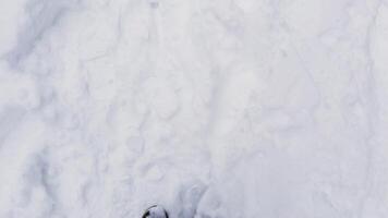 A first-person perspective of someone walking through fresh snow, with winter boots partially covered in snow. Footsteps mark the path, highlighting the cold winter environment video