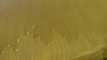 Close-up of thin streams of water creating delicate, jagged patterns as they flow over smooth sand on the shore of Lake Ladoga. Tiny bubbles form along the edges, capturing the natural process of video