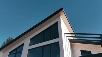 Modern house with sleek design and large windows - A close-up view of a modern wooden house featuring expansive glass windows, a sharp angled roof, and a balcony against a vivid blue sky. video