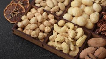 Box with various nuts cashew, macadamia, peanut, cedar, pecan, walnut, brazil, hazelnut on dark textured background video