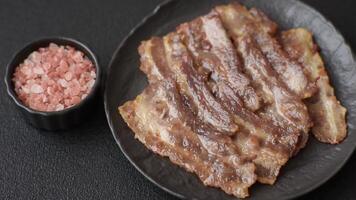 Crispy fried pork bacon sliced with salt, spices and herbs on dark concrete background video