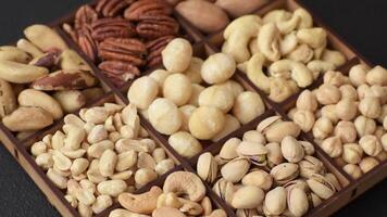 Box with various nuts cashew, macadamia, peanut, cedar, pecan, walnut, brazil, hazelnut on dark textured background video