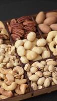 Box with various nuts cashew, macadamia, peanut, cedar, pecan, walnut, brazil, hazelnut on dark textured background video