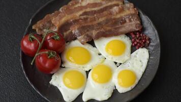 A hearty, delicious breakfast with fried eggs, bacon and tomatoes with salt, spices and herbs video