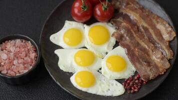 A hearty, delicious breakfast with fried eggs, bacon and tomatoes with salt, spices and herbs video